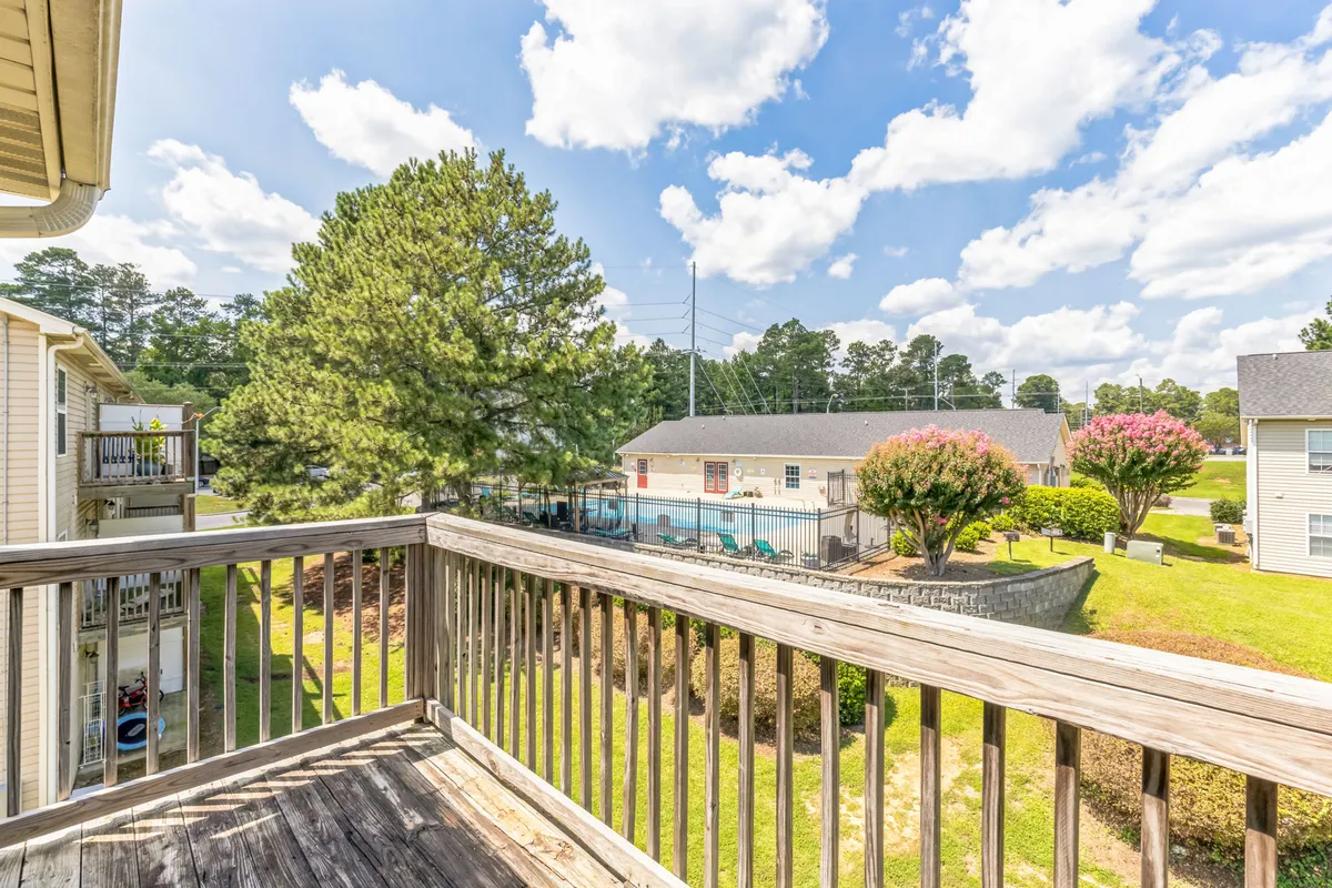 A scenic view from a balcony, overlooking lush greenery, a sparkling swimming pool, and flowering bushes. The tranquil setting suggests a peaceful retreat just steps from urban excitement.