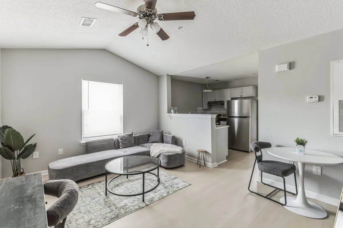 This image showcases an inviting living room featuring a comfortable sofa, a coffee table, and a dining table in the background. The scene suggests both relaxation and opportunities for socializing or dining within the same spacious area. The modern décor and well-chosen furnishings create a welcoming atmosphere that echoes the promise of style and comfort.