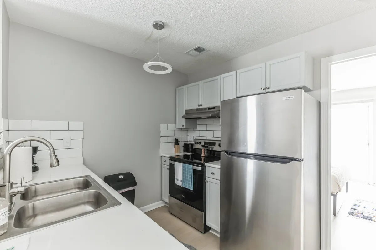 A modern kitchen featuring a stainless steel refrigerator, oven and stove, a sink with a sleek faucet, and expansive clean countertops. The area is bathed in natural light, creating an inviting and functional workspace ideal for meal preparation and entertaining.
