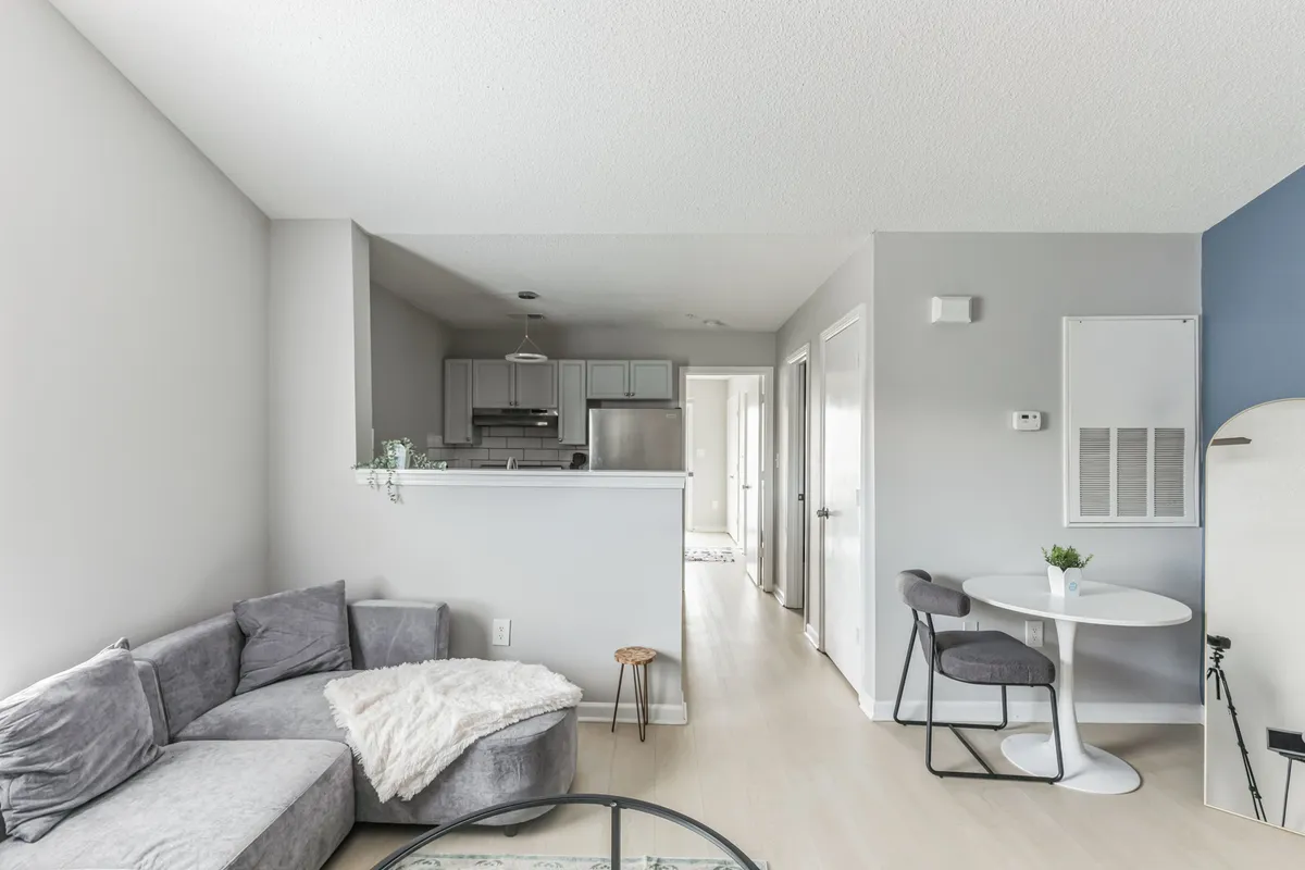 A cozy open-plan space featuring a sectional sofa, dining table, and a visible kitchen area in the background. The inviting setting is ideal for both relaxing and enjoying home-cooked meals, emphasizing the seamless blend of dining and living spaces.