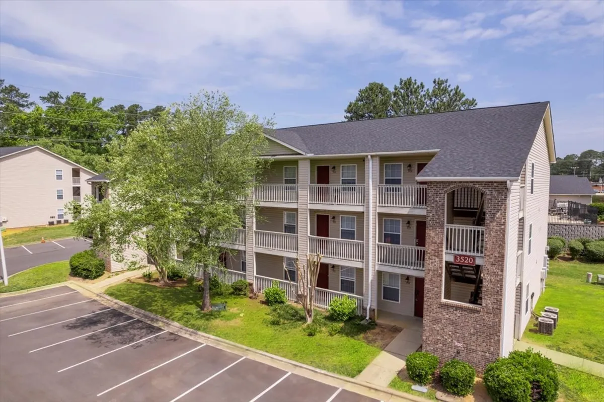 A bright exterior shot showing the building facade, balcony railings, and meticulously landscaped areas. Residents can be seen enjoying the outdoors, socializing on balconies, and walking through the communal spaces.